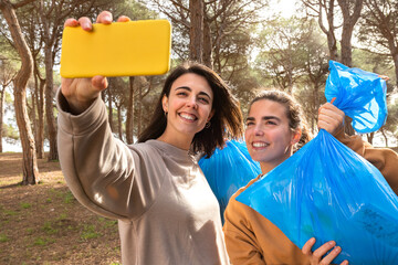 Young caucasian women take selfie with full garbage bags after cleaning the forest.