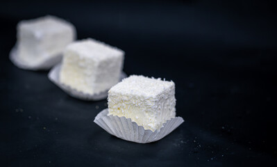 A homemade candy bird's milk with coconut sprinkling on black background.