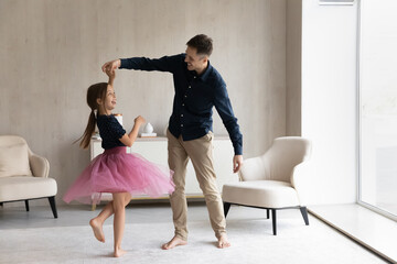 Happy daddy teaching lovely daughter in ballet skirt to dance. Pretty girl wearing princess dress...