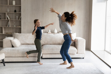 Excited active mom and happy daughter kid having fun, going wild, dancing to music in living room,...