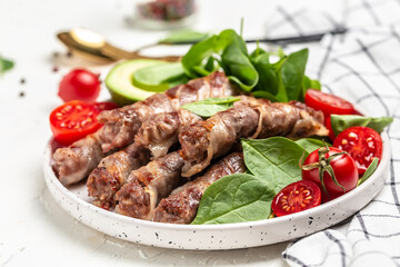 chevapchichi or Kofta kebab, Bacon wrapped minced meat with spinach, avocado and cherry tomato, Healthy fats, clean eating for weight loss. Keto paleo diet menu, top view