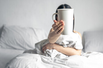 Fototapeta na wymiar A woman holds a cup of coffee while lying in bed.