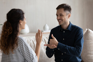 Smiling man and woman with deafness using signs for communication, sitting on couch at home, smiling. Therapist teaching gesture language to patient with disability. Hearing disorder concept © fizkes