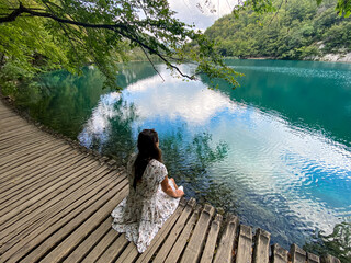 Woman sitting on a wooden path with lakes and waterfalls in the Plitvice Lakes National Park, a...