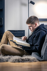 A young man sits in a room and reads the Bible.