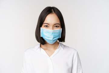 Covid and healthcare concept. Close up portrait of asian woman, office lady in face mask, smiling,...