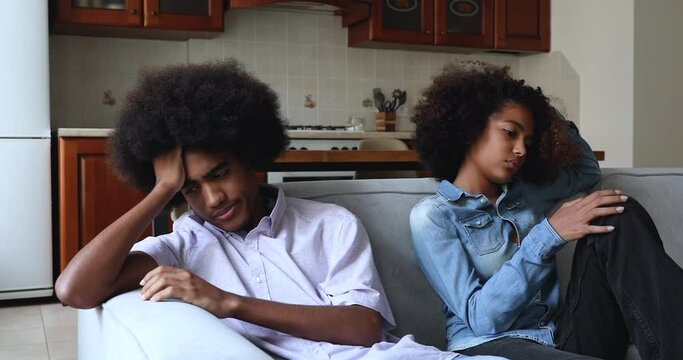 Frustrated African teenagers after fight sit on sofa at home separately. Young couple looking pensive thinks over troubles in relations, having problems in relationships, first love, quarrels concept