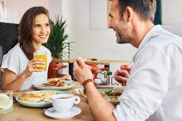 Man and woman eating breakfast at restaurant. Cheerful couple having lunch break at cafe.