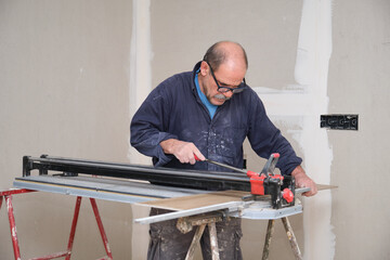 Senior contractor cutting a ceramic wood effect tile with a manual tile cutter to fit the floor....