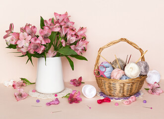 Still life with a basket of needlework and a bouquet of pink alstroemeria flowers on pastel pink background. Spring needlework, crochet as hobby. DIY concept