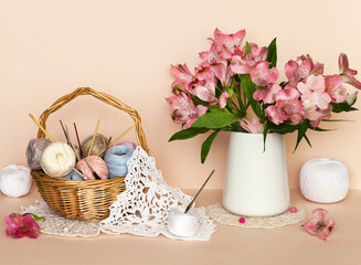 Knitting openwork crochet napkin as gift for 8 March or birthday. Bouquet of pink alstroemeria flowers, crochet hooks, cotton yarn in basket on pastel background. Spring needlework, knitting as hobby