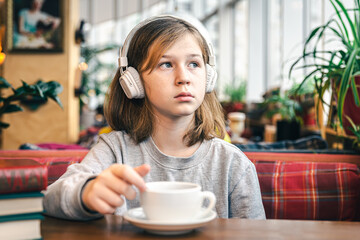 A little girl in headphones in a cafe with a cup of tea.