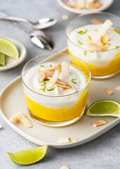 Healthy tropical cream cheese dessert with mango puree and roasted coconut chips in a glass jar....