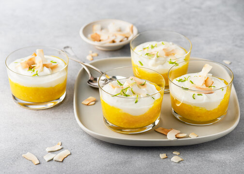 Homemade delicious mango puree and cream cheese layered dessert decorated with roasted coconut chips and grated lime zest on glasses. Healthy food concept.