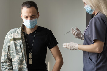 Soldier in uniform receiving vaccine shot against corona virus at the clinic. Military vaccination...