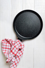 Empty black pan with nonstick surface on white wooden background, vertical view.