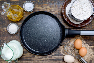 Empty frying pan black with stone nonstick coating for baking pancakes and ingredients on wooden background. Breakfast, top view.