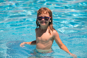 Cute child boy swim in swimming pool, summer water background with copy space. Funny kids face. Summertime and swimming activities for children on the pool.