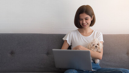 Pretty Asian woman working on laptop while holding cute small white maltese breed dog. Work from home, study online during lock down.