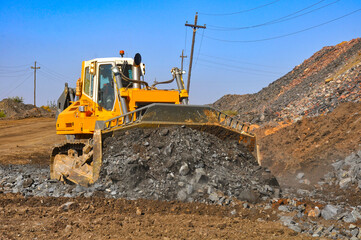Obraz premium Bulldozer working in an iron ore quarry. Bulldozer clears the road from the rock mass. Buddozer builds a road in a quarry.