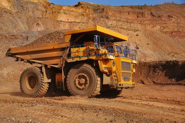 Mining dump truck transports rock, iron ore along the side of the quarry.