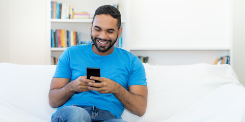 Handsome latin american hipster man with beard sending message at mobile phone