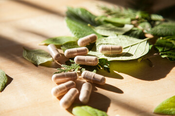 Obraz na płótnie Canvas Beige vitamin medicine pills on wooden table with green leafs and window sunlight