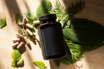 blank label black bottle with beige vitamin medicine pills on wooden table with green leafs and...