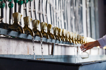 Water purification station. Pipes and vintage Soviet brass taps (in focus left). Chemist take sample of purified water in flask (out of focus, hand only). Short depth of field. Kyzylorda, Kazakhstan.
