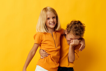 Boy and girl in yellow t-shirts standing side by side childhood emotions yellow background