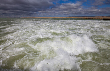 Small Aral Sea Kok-aral dam. Turbulent water after dam. Blue sky with clouds on horizon. Kzylorda region, Kazakhstan.