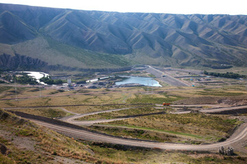 Fototapeta premium Second dam on Charyn (Sharyn) river. Asphalt roads, bridge, orange truck. Small lake. Green mountains on background.