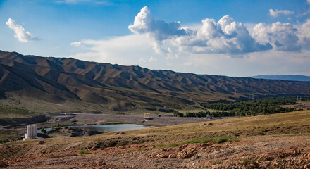Scenic view of second dam on Sharyn river. Asphalt road and bridge. Small lake. Green mountains on background. Blue sky, clouds.