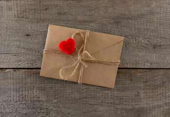 brown envelope tied with a linen rope and a red velvet heart on a wooden background.