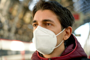 Close up of man wearing medical mask FFP2 KN95 at train station staring away. Blurred background....