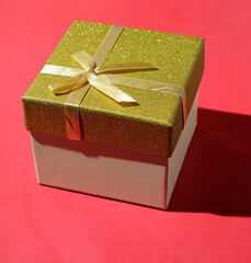 Gift box decorated with golden bow on red  background copy space
