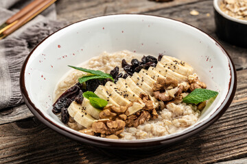 Oatmeal. Porridge with dried raisins, banana and walnuts decorated with mint for healthy breakfast or lunch. Natural ingredients. Clean eating, dieting, vegan food concept. top view