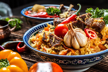 Traditional uzbek meal called pilaf. Rice with meat on plate with oriental ornament on a dark wooden background, Long banner format. space for text
