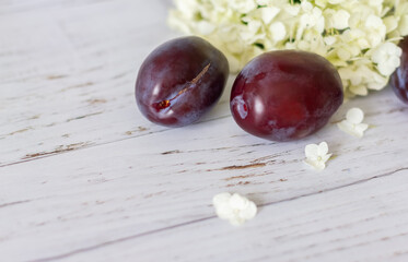Ripe plums on a wooden background, hydrangea flowers lie nearby.