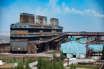 Fototapeta premium Rusted industrial building of metal alloy plant (smelter) with chimneys (smoke stacks) and pipes. Blue sky background.
