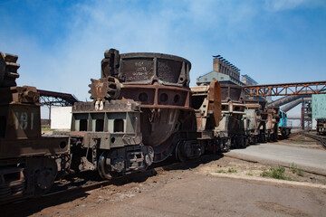 Fototapeta na wymiar Metal alloys plant (smelter). Train on rails. Blue locomotive and rusted wagon. Metallurgical plant main industrial building on background.