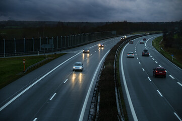 Fototapeta na wymiar Driving cars on a wet highway at dusk under a cloudy sky in Germany, motion blur, copy space, selected focus
