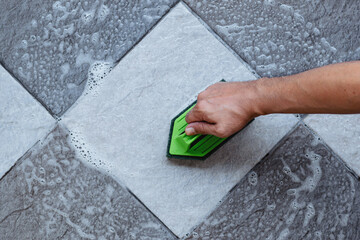 Top view of a human hand are using a green color plastic floor scrubber to scrub the tile floor...