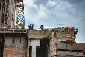 Demolition of old outdated Soviet cement plant. Workers on the roof. Grey sky with storm clouds. Temirtau, Kazakhstan.