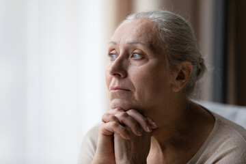 Thoughtful bored older 70s woman looking at window, feeling depressed, frustrated, lonely,...