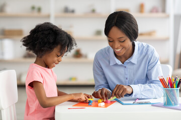 Adorable little black girl and teacher playing with play dough