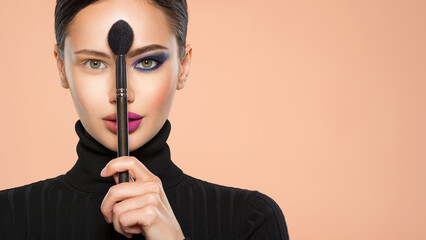 Portrait of a girl with cosmetic brush at face. Woman holds a big makeup brush right in the middle...