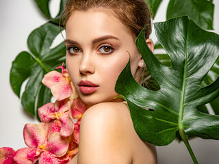 Closeup girl's face with green leave. Model with pink tropical orchid near face. Pretty girl in...