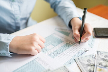 Close-up of a woman filling out a 1040 form while sitting at a table. Tax concept