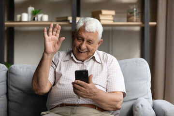 Happy friendly senior 80s grandpa man speaking on video conference call on smartphone, waving...